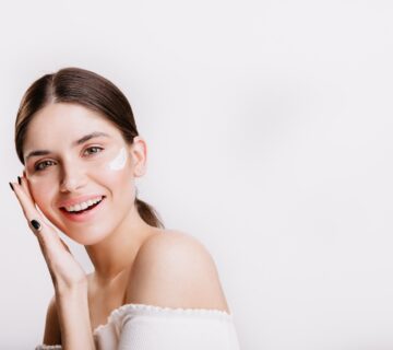 Girl touches moisturized skin smiles portrait model with cream face isolated wall 2000px 360x320