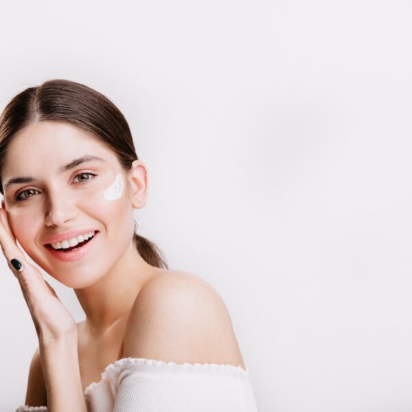 Girl touches moisturized skin smiles portrait model with cream face isolated wall 2000px 600x600