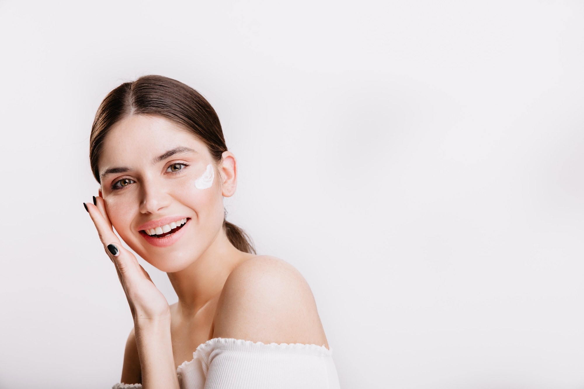 Girl touches moisturized skin smiles portrait model with cream face isolated wall 2000px